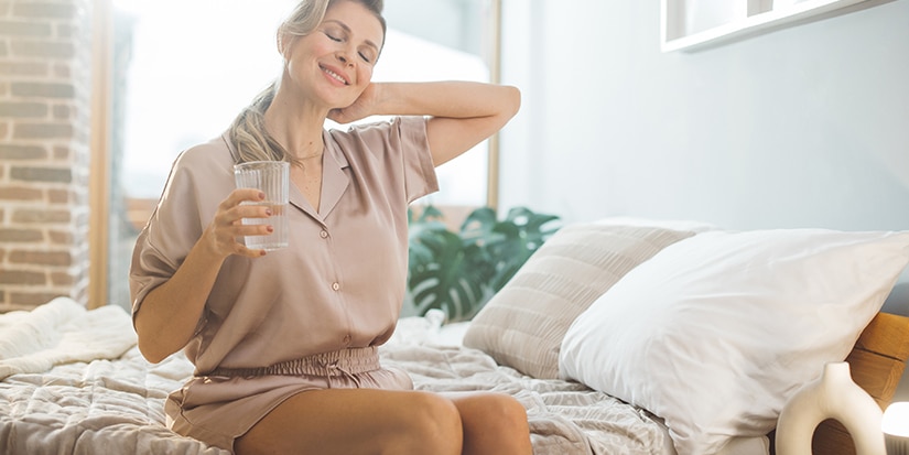 Woman enjoying a calm morning while holding a glass of water, representing wellness and balanced lifestyle at Essential Health Bozeman NC.