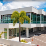 Modern commercial building featuring expansive glass windows, clean architectural lines, palm trees, and convenient on-site parking.